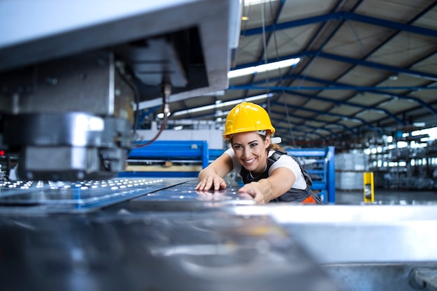 Gratis foto vrouwelijke fabrieksarbeider in beschermende uniform en veiligheidshelm industriële machine op productielijn