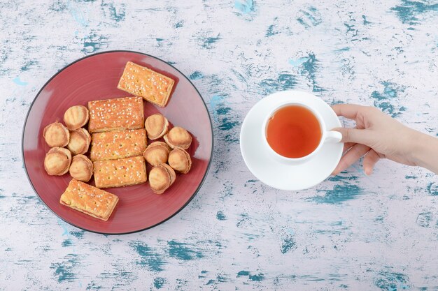 Vrouwelijke hand met een kopje thee met zandkoek noten met gecondenseerde melk.