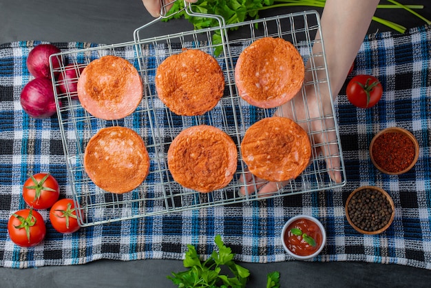 Gratis foto vrouwelijke hand met gegrilde salami plakjes op grill rooster over verse groenten.