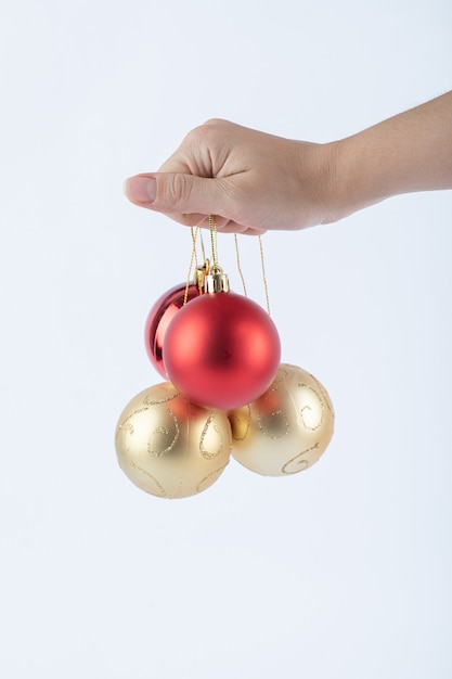 Vrouwelijke hand met glanzende kerstballen op witte ondergrond