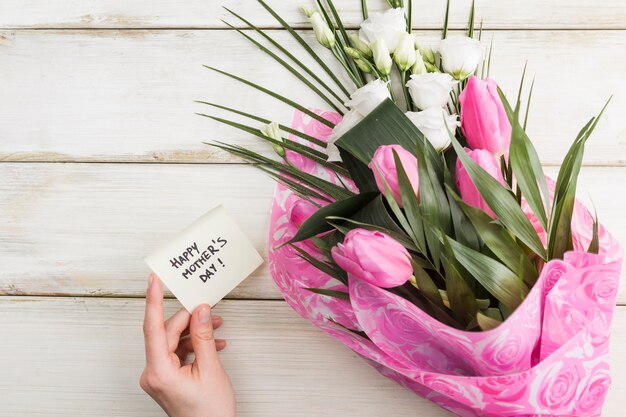 Vrouwelijke hand met vakantiekaart en boeket bloemen