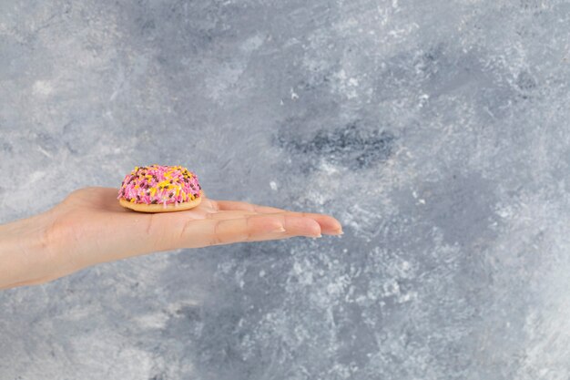 Vrouwelijke hand met vers koekje met kleurrijke hagelslag op stenen oppervlak