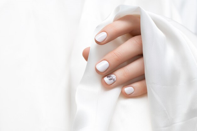 Vrouwelijke hand met witte paardebloem nagel ontwerp.