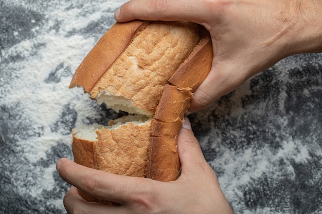 Vrouwelijke handen breken vers gebakken brood, close-up bovenaanzicht.