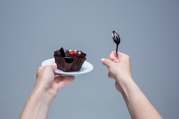 Vrouwelijke handen die cake met lepel op grijs houden