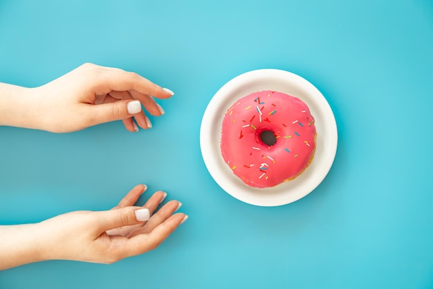 Vrouwelijke handen en donut op een blauwe achtergrond plat leggen