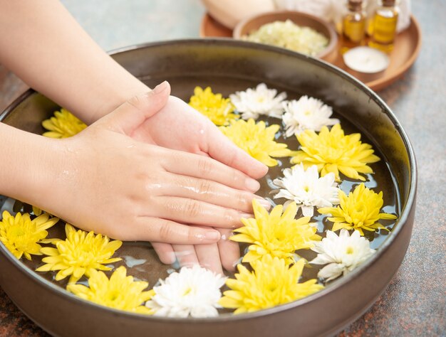 Vrouwelijke handen en kom met spa-water met bloemen, close-up. Hands Spa.