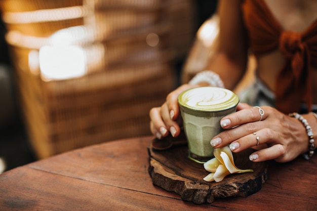 Vrouwelijke handen met zilveren ringen houdt een glas matcha latte vast