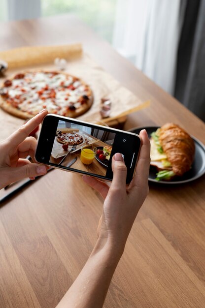 Vrouwelijke handen nemen foto van een gesneden pizza en een glas sinaasappelsap