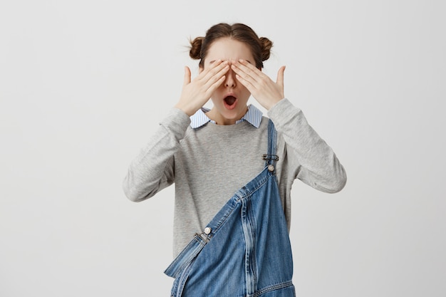 Vrouwelijke hipster die ogen behandelen met handen die emotioneel op gelukwensen reageren. Knappe vrouw die op iets met gesloten ogen anticipeert terwijl status over blinde muur. Lichaamstaal