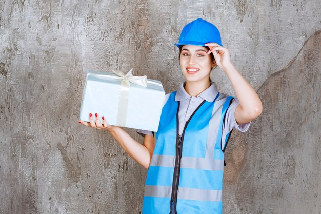 Vrouwelijke ingenieur in blauw uniform en helm met een blauwe geschenkdoos.