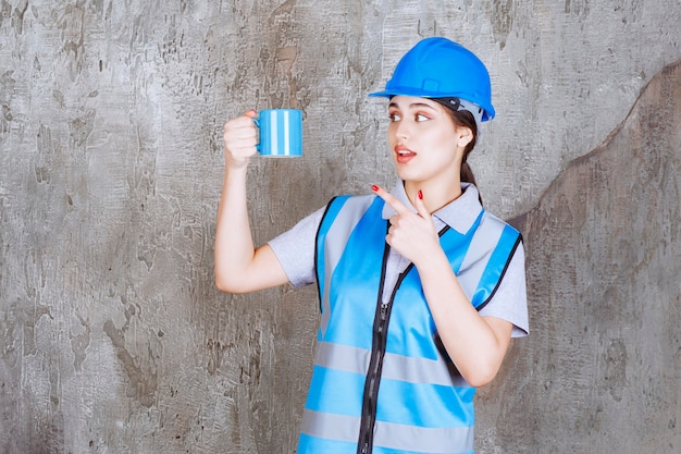 Vrouwelijke ingenieur in blauw uniform en helm met een blauwe theekop.