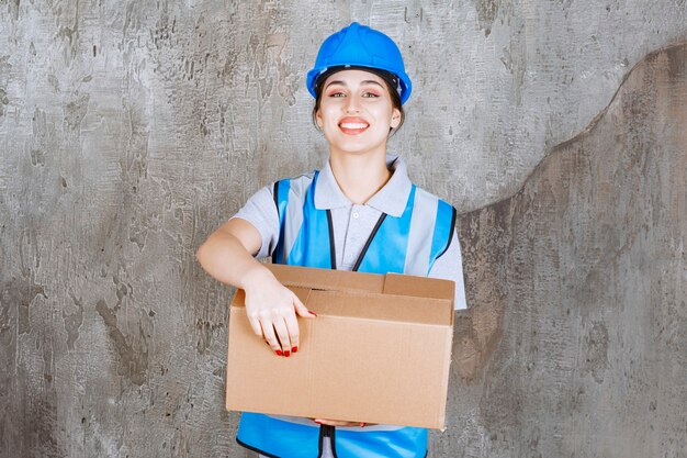 Vrouwelijke ingenieur in blauw uniform en helm met een kartonnen pakket.