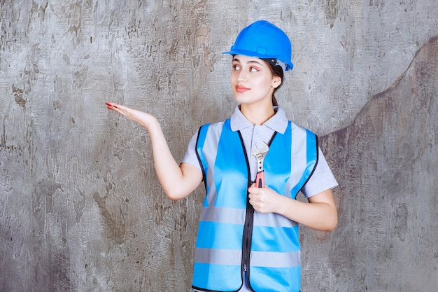 Vrouwelijke ingenieur in blauw uniform en helm met een metalen moersleutel.