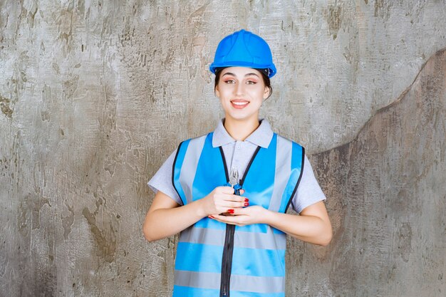 Vrouwelijke ingenieur in blauwe versnelling en helm met tang voor reparatiewerkzaamheden.