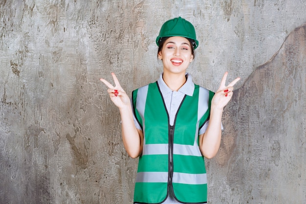 Vrouwelijke ingenieur in groen uniform en helm die vrede en vriendschap verzendt