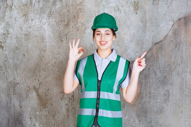 Vrouwelijke ingenieur in groen uniform en helm met positief handteken