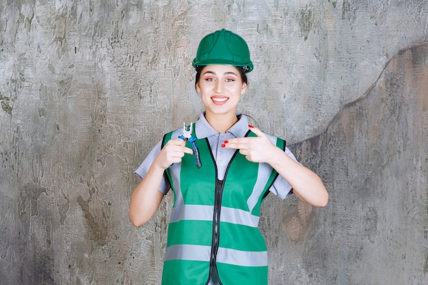 Vrouwelijke ingenieur in groene helm die een tang vasthoudt voor reparatiewerkzaamheden