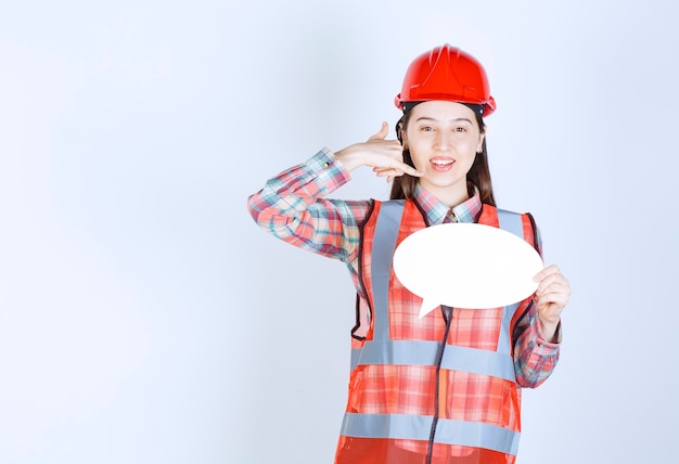Vrouwelijke ingenieur in rode helm die een leeg infobord vasthoudt en om een oproep vraagt.
