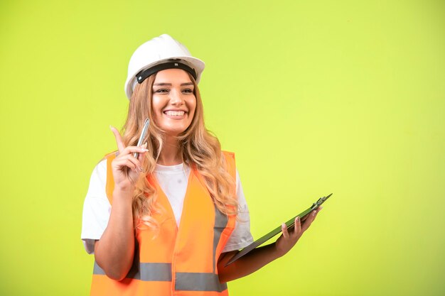 Vrouwelijke ingenieur in witte helm en uitrusting houdt de checklist vast en voelt zich zelfverzekerd.