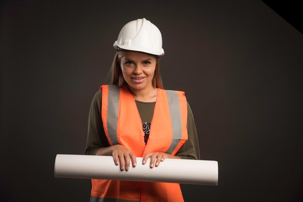 Vrouwelijke ingenieur met een witte helm die het projectplan aanbiedt en er professioneel uitziet.
