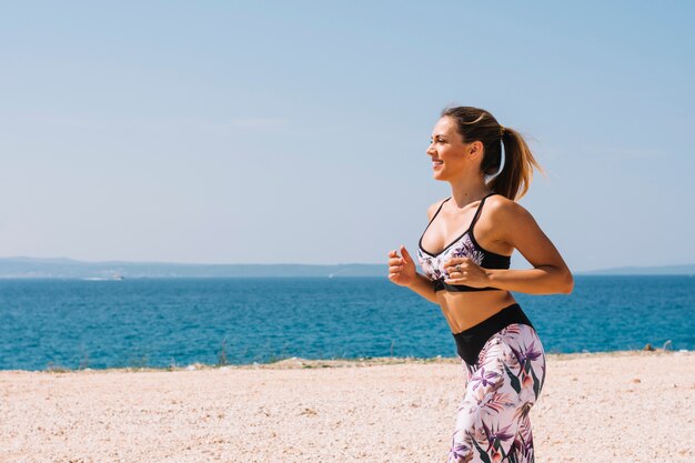 Vrouwelijke jogger die dichtbij het overzees bij strand loopt