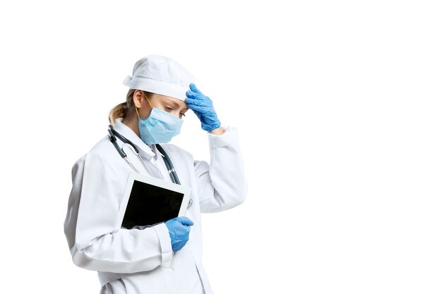 Vrouwelijke jonge arts met stethoscoop en gezichtsmasker dat op witte muur wordt geïsoleerd