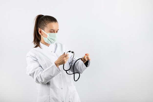 Vrouwelijke jonge dokter in wit uniform die naar een stethoscoop kijkt