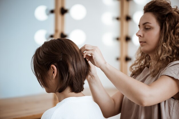 Vrouwelijke kapper die kapsel maakt aan donkerbruine vrouw in schoonheidssalon