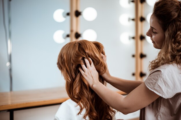 Vrouwelijke kapper die kapsel maken aan roodharigevrouw in schoonheidssalon