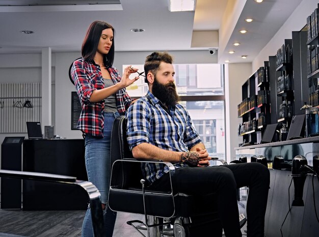 Vrouwelijke kapper knippen haar van bebaarde hipster man in een salon.