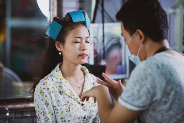 vrouwelijke kapper permanent, gezicht make-up en het maken van kapsel tot schattige mooie jonge vrouw in schoonheidssalon