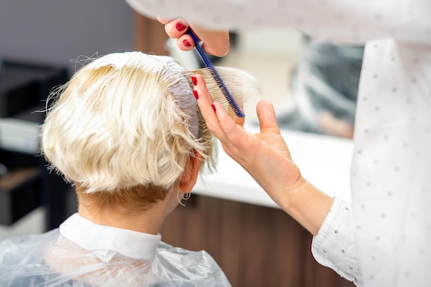 Vrouwelijke kapper styling kort wit haar van de jonge blonde vrouw met handen en kam in een kapsalon.