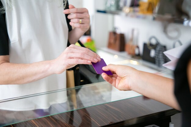 Vrouwelijke klant die voor aankoop met creditcard in kledingwinkel betaalt, lege kaart aan kassier over bureau geeft. Bijgesneden schot, close-up van handen. Winkelen of kopen concept
