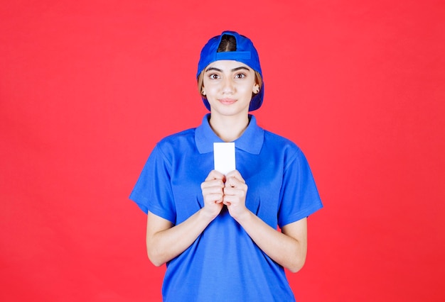 Vrouwelijke koerier die in blauw uniform haar visitekaartje voorstelt.