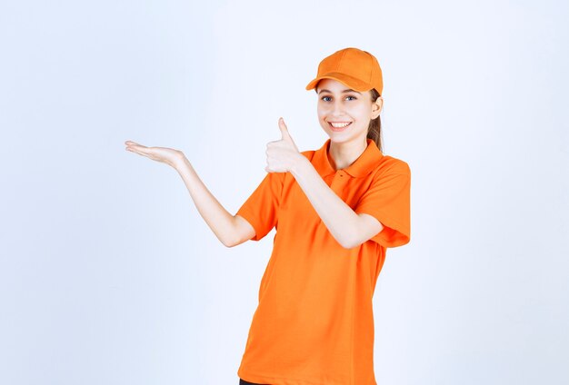 Vrouwelijke koerier die oranje uniform en GLB draagt die duim toont.