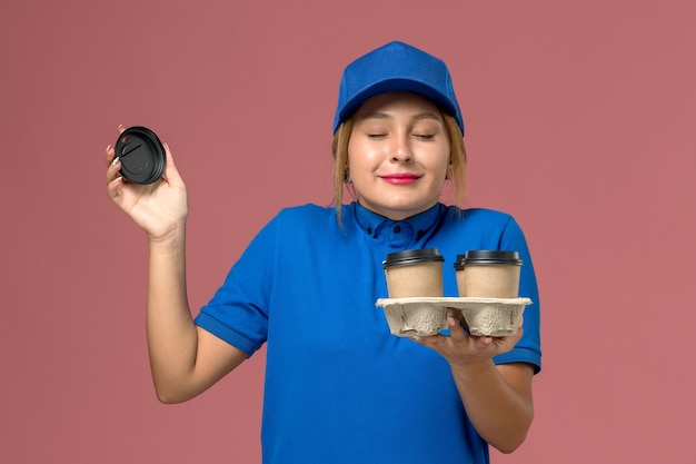 vrouwelijke koerier in blauw uniform bedrijf levering kopjes koffie ruiken ze op roze, service werknemer uniforme levering