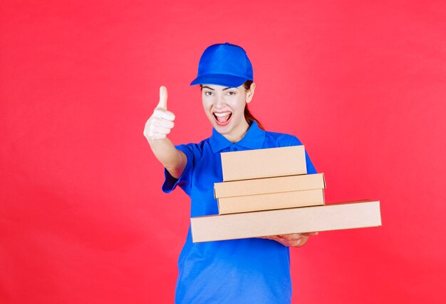 Vrouwelijke koerier in blauw uniform met een voorraad kartonnen dozen en een teken van plezier