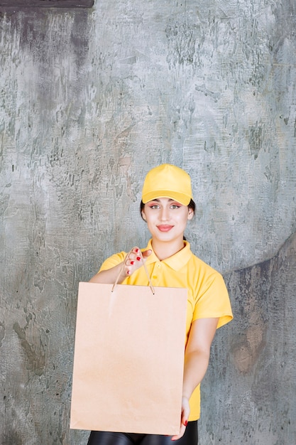 Vrouwelijke koerier in geel uniform die een kartonnen boodschappentas aflevert.