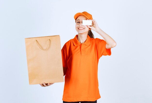 Vrouwelijke koerier in geel uniform levert een boodschappentas en presenteert haar visitekaartje