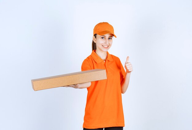 Vrouwelijke koerier in oranje uniform die een afhaalpizzadoos vasthoudt en een positief handteken toont