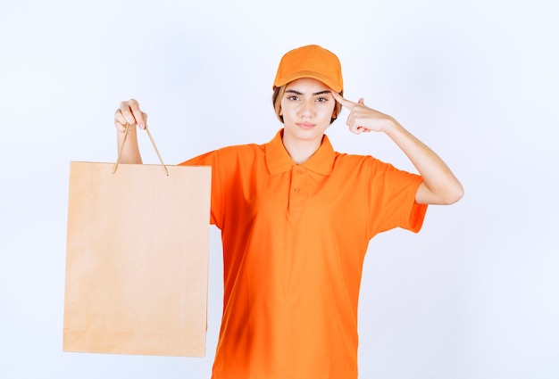 Vrouwelijke koerier in oranje uniform die een kartonnen boodschappentas aflevert en er attent uitziet