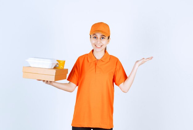 Vrouwelijke koerier in oranje uniform met een kartonnen doos, een plastic afhaaldoos en een gele noedelbeker