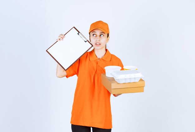 Vrouwelijke koerier in oranje uniform met een kartonnen doos en een plastic afhaaldoos erop en vraagt om een handtekening.