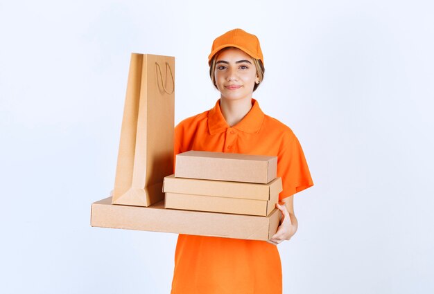 Vrouwelijke koerier in oranje uniform met een voorraad kartonnen pakjes en boodschappentassen