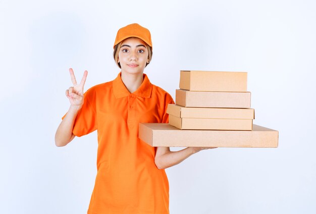 Vrouwelijke koerier in oranje uniform met een voorraad kartonnen pakjes en ziet er positief uit