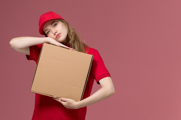 vrouwelijke koerier in rood uniform bedrijf levering voedsel doos op lichtroze, uniform baan service werknemer levering meisje