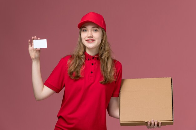 vrouwelijke koerier in rood uniform bedrijf levering witte kaart voedseldoos op lichtroze, uniform baan service werknemer levering meisje