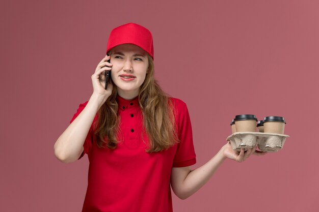 vrouwelijke koerier in rood uniform koffie houden en praten aan de telefoon op roze, baan uniforme werknemer dienstverlening