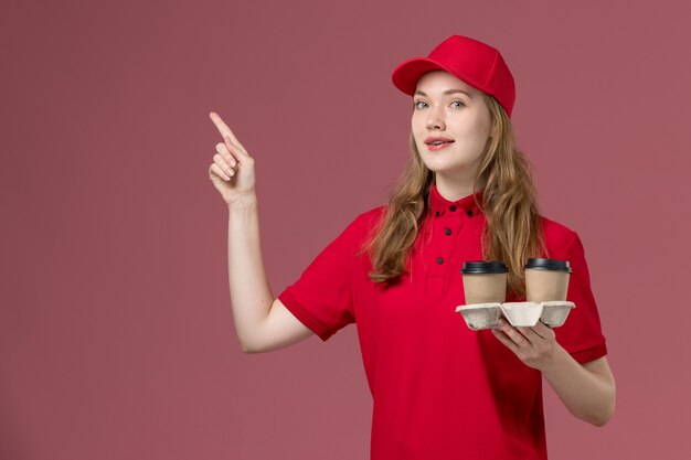 vrouwelijke koerier in rood uniform met bruine koffiekopjes op roze, uniforme dienstverlener